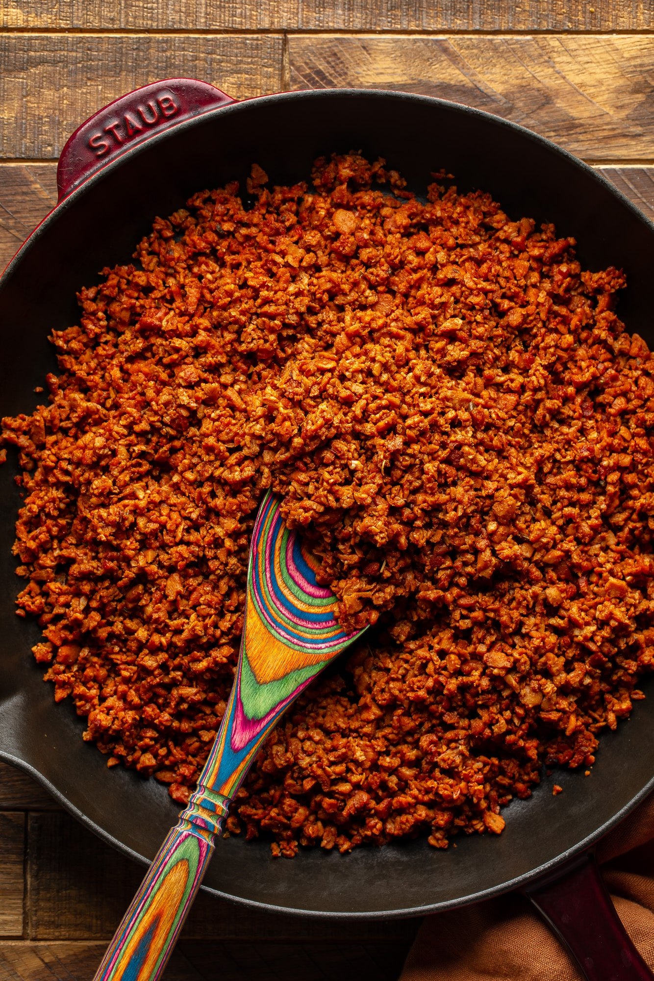 Using a wooden spoon to stir the vegan sausage in a large pan.