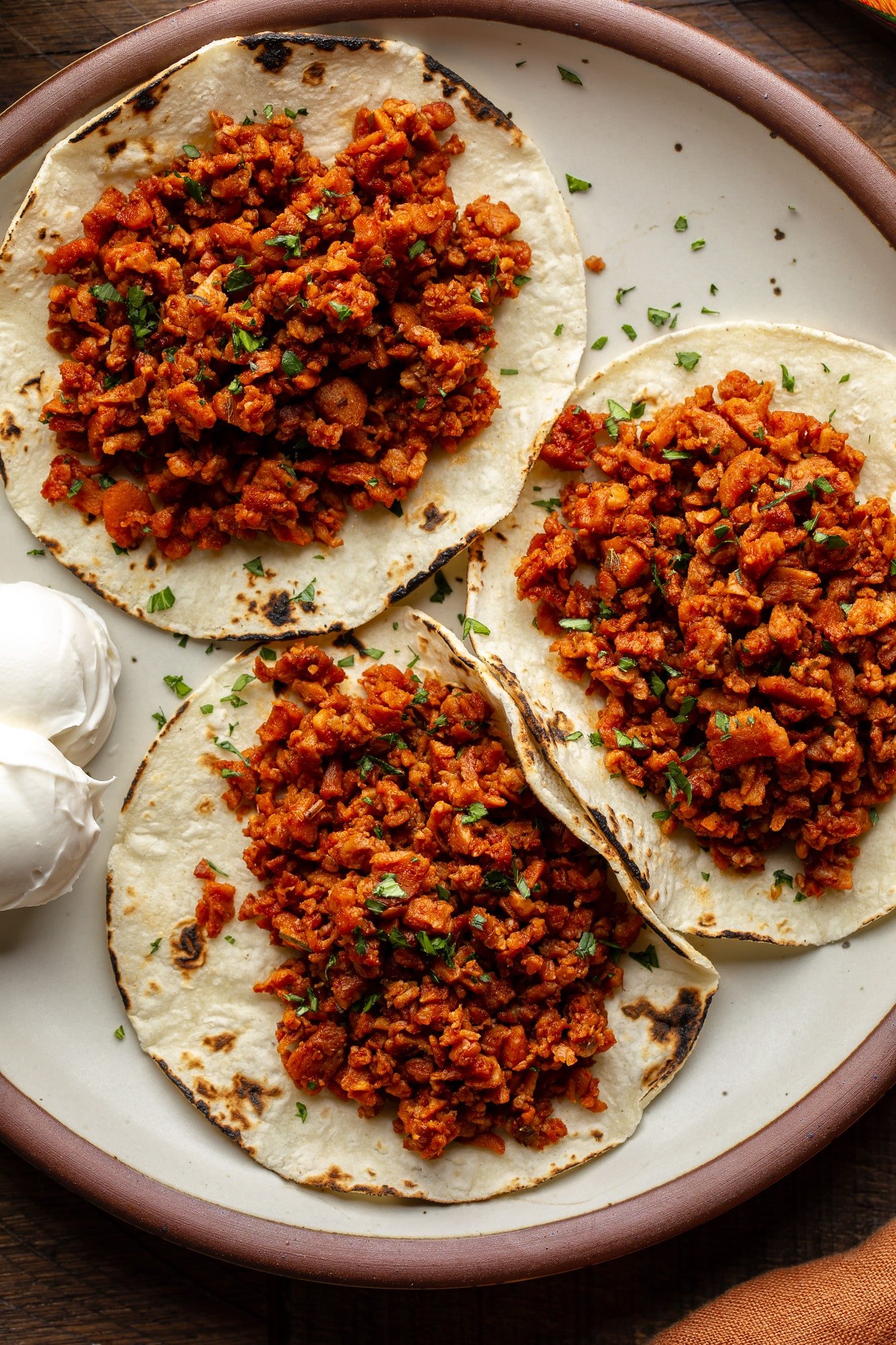 Three tortillas finished off with vegan sausage on a plate.